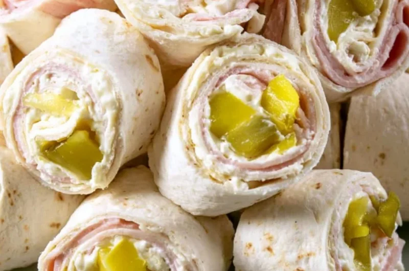 Cozy Pickle Dip Pinwheels served on a wooden platter with fresh herbs.